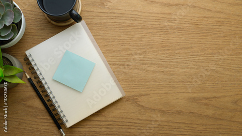 Top view of notebook, pencil, sticky note, coffee cup and copy space on wooden table