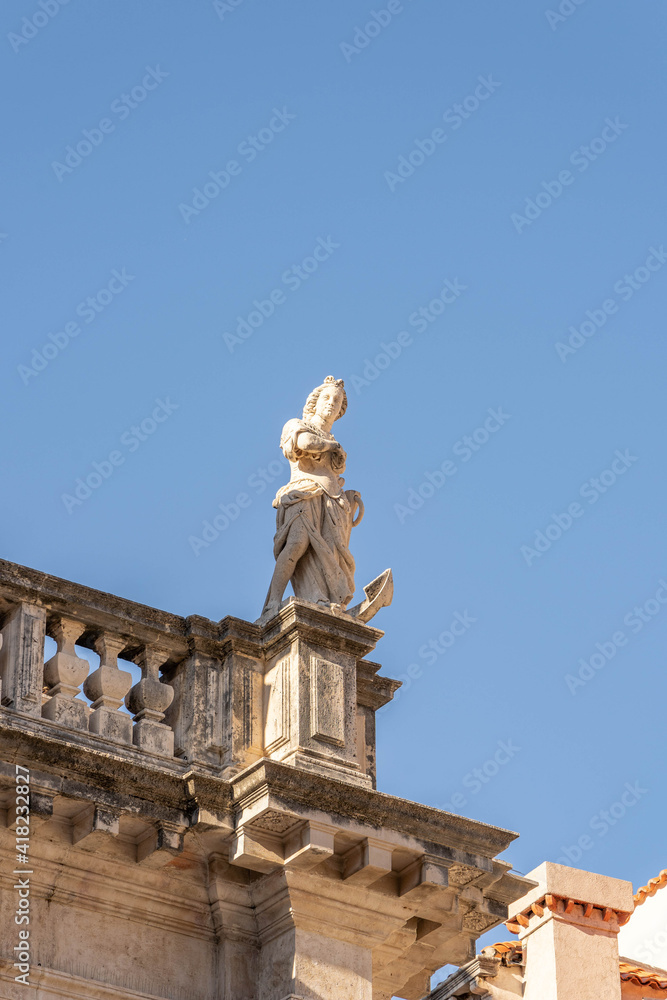 Marble statue of goddess on top of building on stradun street in old town Dubrovnik in summer morning