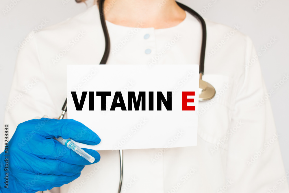 The doctor's blue - gloved hands show the word VITAMIN E - . a gloved hand on a white background. Medical concept. the medicine The doctor's blue - gloved hands show the word VITAMIN E - . a gloved hand on a white background. Medical concept. the medicine
