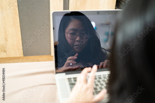 The reflection of Beautiful Asian woman from laptop screen. She plays laptop and lays on the bed in her bedroom. photo