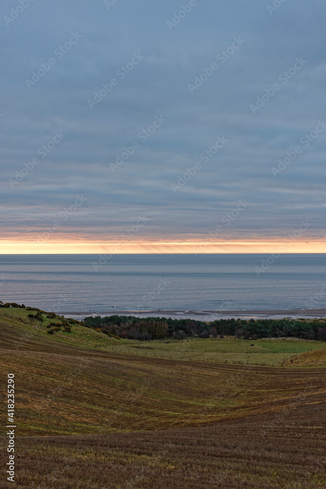 The sun rising beneath the Low Cloud layer over Lunan bay and the rolling Farmland behind the beach on an early morning in February. The sun rising beneath the Low Cloud layer over Lunan bay and the rolling Farmland behind the beach on an early morning in February.