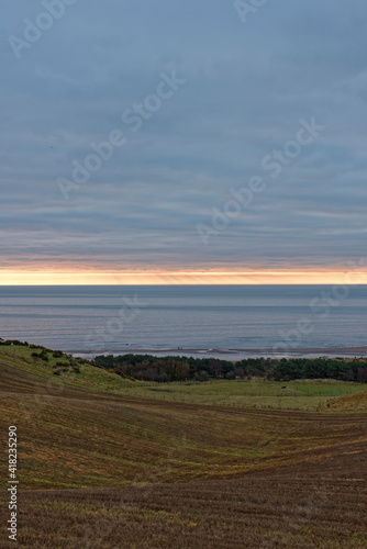 The sun rising beneath the Low Cloud layer over Lunan bay and the rolling Farmland behind the beach on an early morning in February.