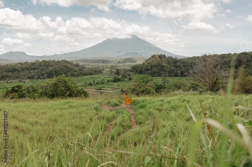 Young girl walking in rice field in Ubud, Bali, barefoot, wearing long yellow dress and look at Agung volcano photo