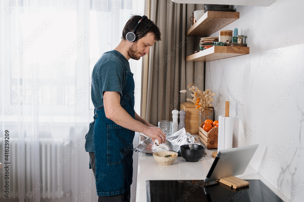 Obraz premium Adult man making dorado fish by video recipe and listening to social media audio chat on headphones