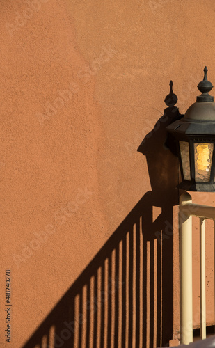 dark black shadow on orange concrete wall created by lamp and stair railing on sunny day in afternoon sun low in sky angles vertical striped lines on bare cement wall room for type open space vertical photo