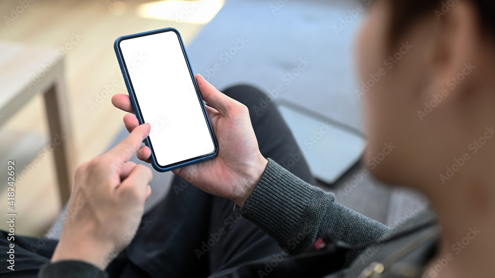Close up view of young man holding mobile phone with empty screen while sitting on sofa at home. Close up view of young man holding mobile phone with empty screen while sitting on sofa at home.
