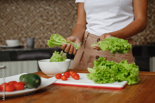 Cropped image unrecognisable woman cooking healthy food at home kitchen - lettuce salad, cherry toatoes and cucumber