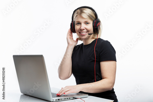 Smiling young woman with headphones, microphone with laptop. Blonde in a black T-shirt. Distance education, remote work and support service. White background. Space for text.