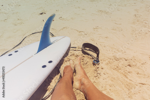  Woman feet legs next white surfboard with blue fin lying on sand beach in sunny day, Australia, Sunshine Coast, Queensland holiday concept
