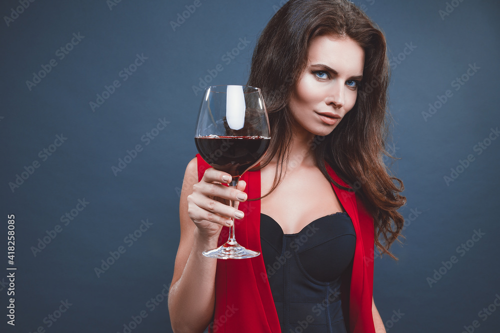 Woman with bright makeup, hairstyle wearing red dress posing with glass of vine over dark background, isolate. Woman with bright makeup, hairstyle wearing red dress posing with glass of vine over dark background, isolate.