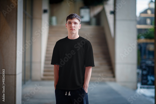 Black T-shirt template for a guy, against the background of a blurred building, urban style of clothing, for advertising in an online store.