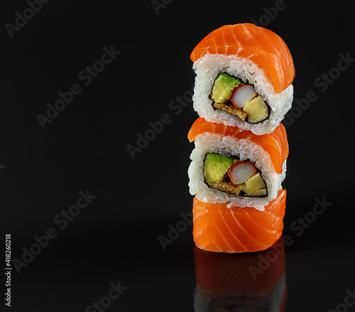 Balancing fresh sushi rolls on a black background with reflection. Japanese kitchen, restaurant, copy space. photo