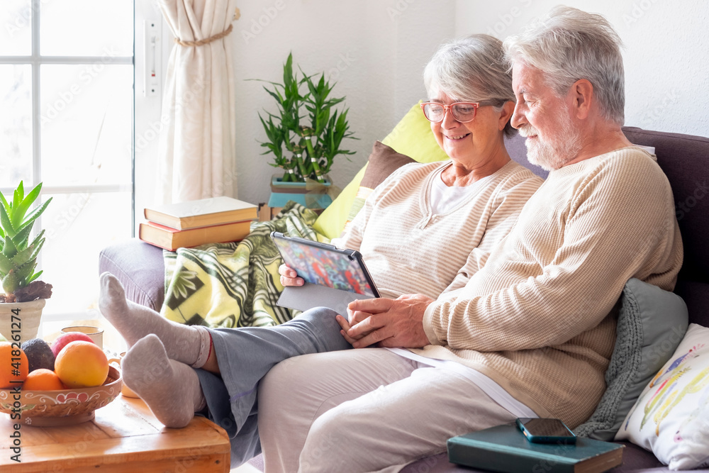 Senior couple relaxing on sofa at home looking together at digital tablet and smiling