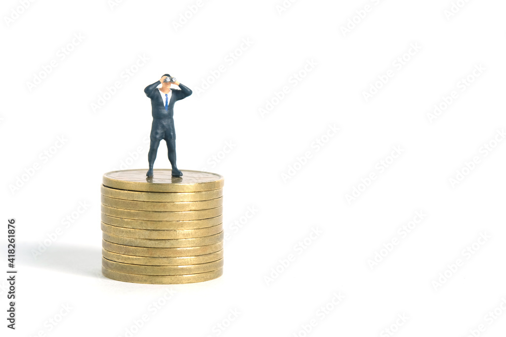 Miniature people toys photography. A businessman looking, searching, observing using binoculars above gold money coin stack isolated on white background. Miniature people toys photography. A businessman looking, searching, observing using binoculars above gold money coin stack isolated on white background.