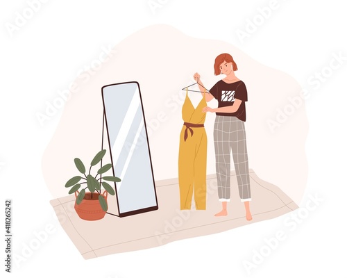 Young woman in home clothes holding fashion outfit on hanger rack and prepari...
