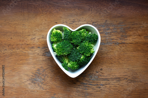 Fresh cut broccoli in heart shape bowl on rustic wooden background