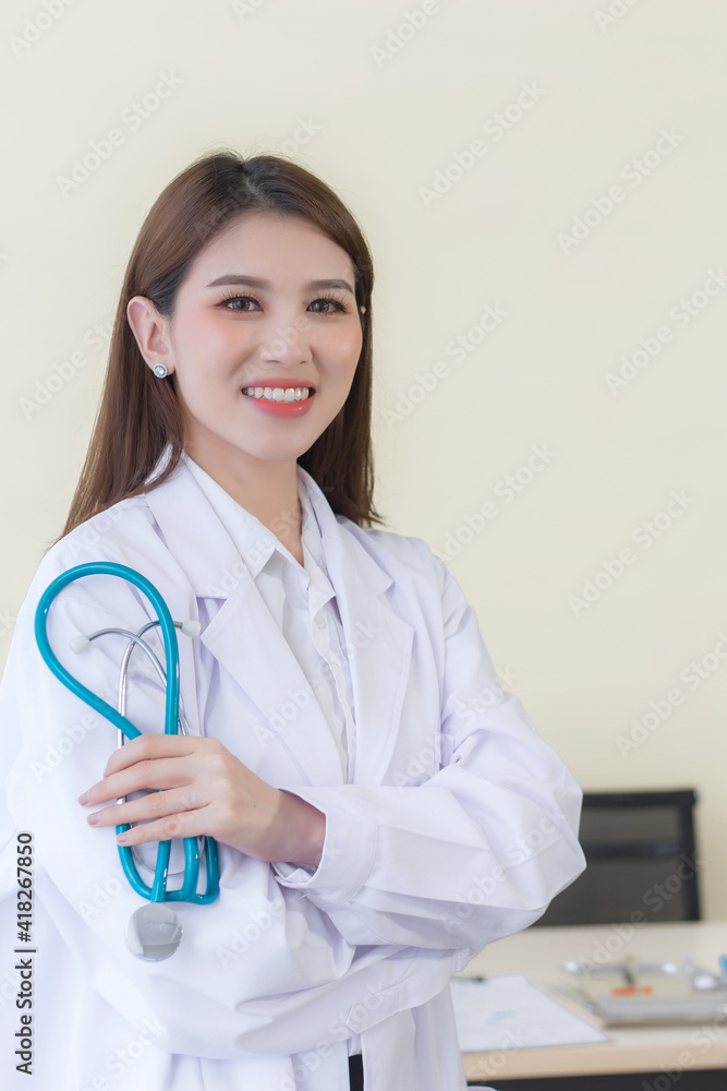 Young beautiful Asian woman doctor Standing with arms crossed happy and smile in hospital. Wearing a white robe and stethoscope. Health care concept. Young beautiful Asian woman doctor Standing with arms crossed happy and smile in hospital. Wearing a white robe and stethoscope. Health care concept.