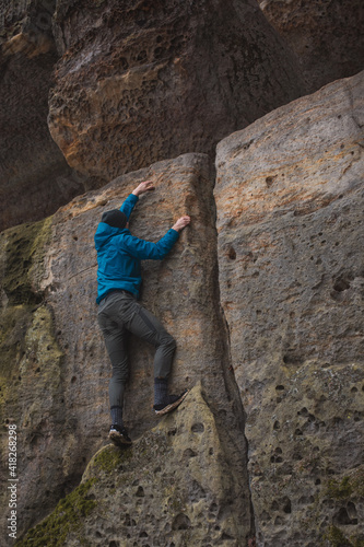 man in a blue jacket climbing a stone wall holding with strong hands in a crack in the stone wall