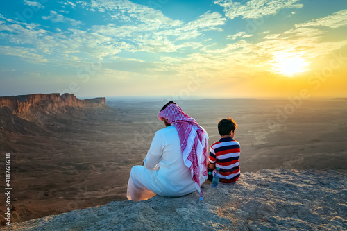 Obraz na plátně An arab man and his son sitting on Edge of the world, a natural landmark and popular tourist destination near Riyadh -Saudi Arabia