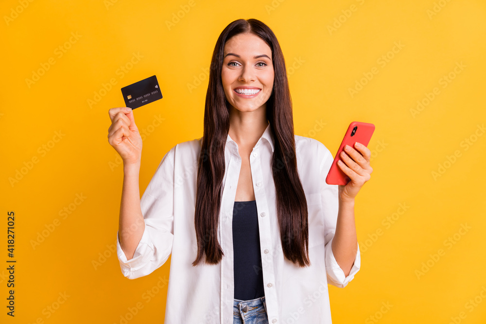 Portrait of cheerful friendly lady hold debit card phone toothy smile isolated on yellow color background Portrait of cheerful friendly lady hold debit card phone toothy smile isolated on yellow color background