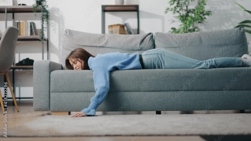Tired young woman lying comfortably on grey couch at bright living room. Relaxation after hard long day. Cozy atmosphere at home. Tired young woman lying comfortably on grey couch at bright living room. Relaxation after hard long day. Cozy atmosphere at home.