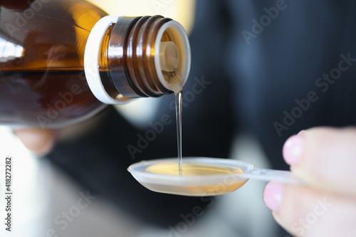 Woman pouring medicinal syrup into measuring spoon closeup photo