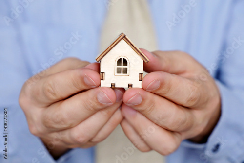Real estate agent, wooden house in male hands. Man in office clothes with house model, purchase or rental home
