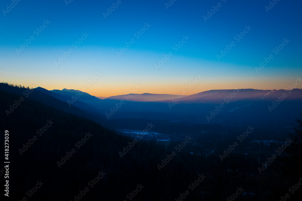 Clear blue sky over Podhale region, Poland. Orange sunset illuminates the ridge of Tatra Mountains. Selective focus on the silhouette of the hills, blurred background.