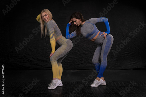 athletic girls in tight fitness clothes posing against a dark background © Дмитрий Хитрин