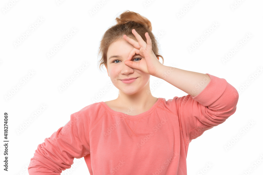 Close up optimistic teen girl showing OK sign over eye while standing isolated white background Close up optimistic teen girl showing OK sign over eye while standing isolated white background