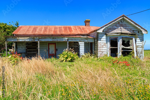 A derelict, abandoned villa-style farmhouse in New Zealand, with colorful flowers still growing in the garden
