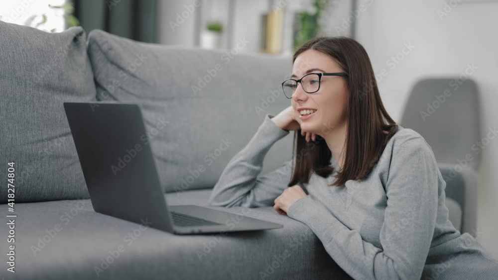 Attractive young woman in eyeglasses using laptop for video chat while staying at home. Pretty lady in casual wear talking during online conference on portable computer. Attractive young woman in eyeglasses using laptop for video chat while staying at home. Pretty lady in casual wear talking during online conference on portable computer.