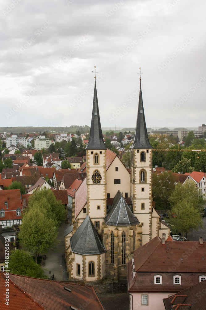 Bad Wimpfen church, cloistered between the red-roofed half-timbered houses, with two symmetrical pointed towers on a cloudy day.