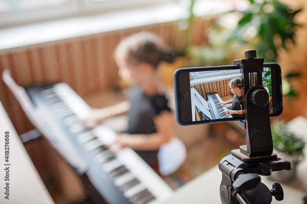 Pretty young musician in classic black dress playing digital piano at home during online concert and recording video, social distance during quarantine, online education concept, video blogging