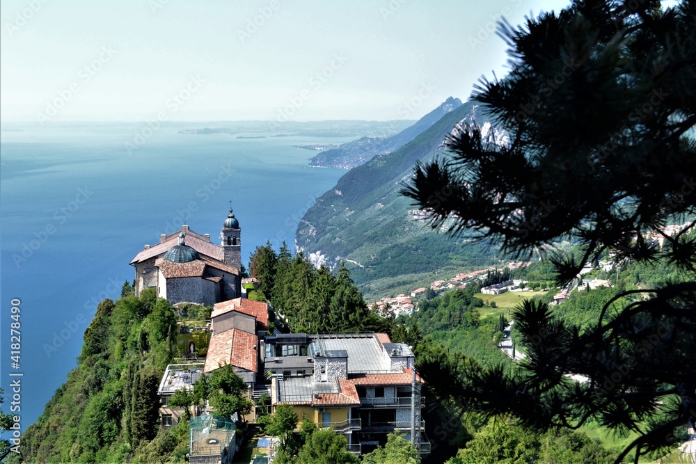 View of the lake from the top of the mountain. Old church and trees in the foreground.  Lake Garda Italy