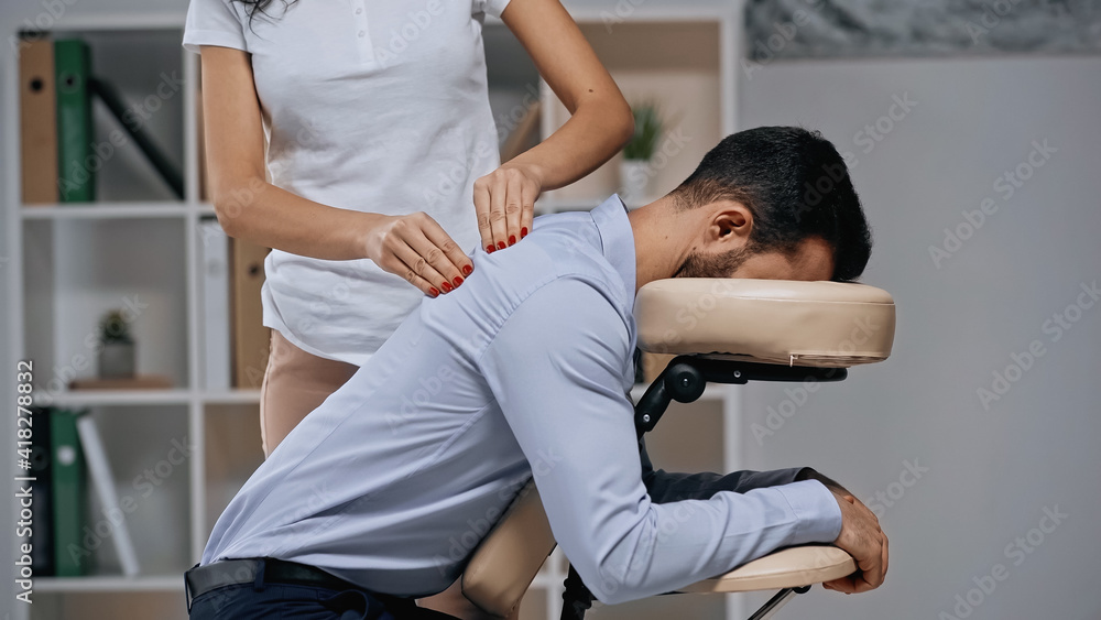 Fototapeta premium Masseur massaging back of businessman on massage chair in office
