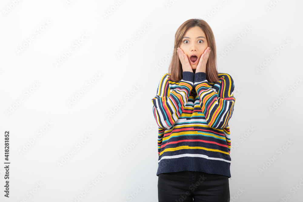 A young lady holding hands near cheeks in sweater and looking at camera A young lady holding hands near cheeks in sweater and looking at camera