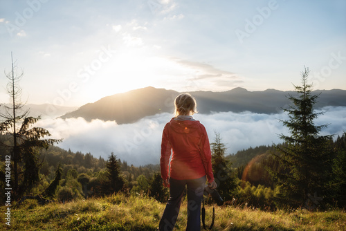  Girl tourist with a camera at dawn in the mountains. beautiful sunrise in the mountains with fog and shining sun over the mountain tops.