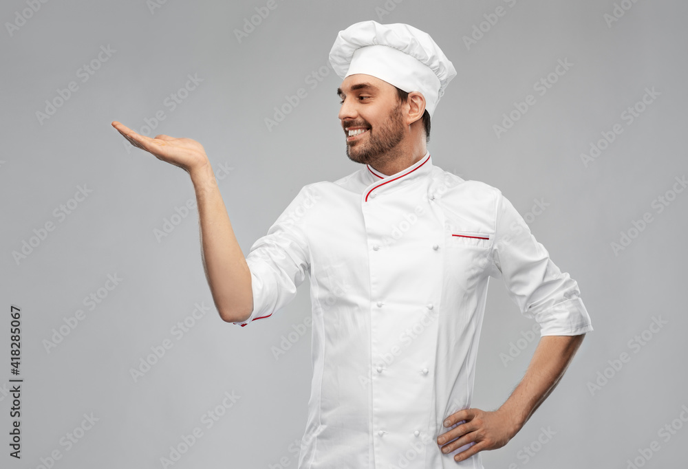 cooking, culinary and people concept - happy smiling male chef in toque holding something on hand over grey background cooking, culinary and people concept - happy smiling male chef in toque holding something on hand over grey background