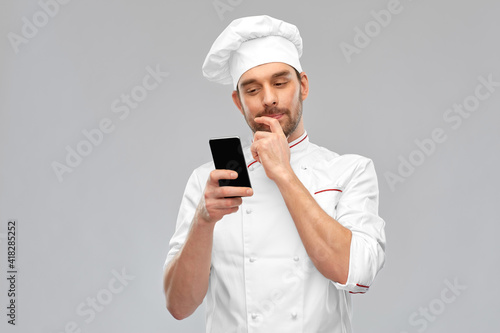 cooking, culinary and people concept - male chef in toque with smartphone over grey background