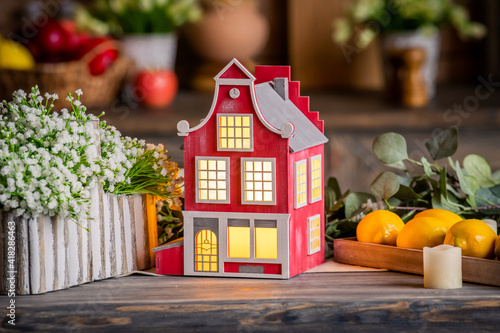 toy decorative lamp house stands on wooden table among spring flowers and interior elements.