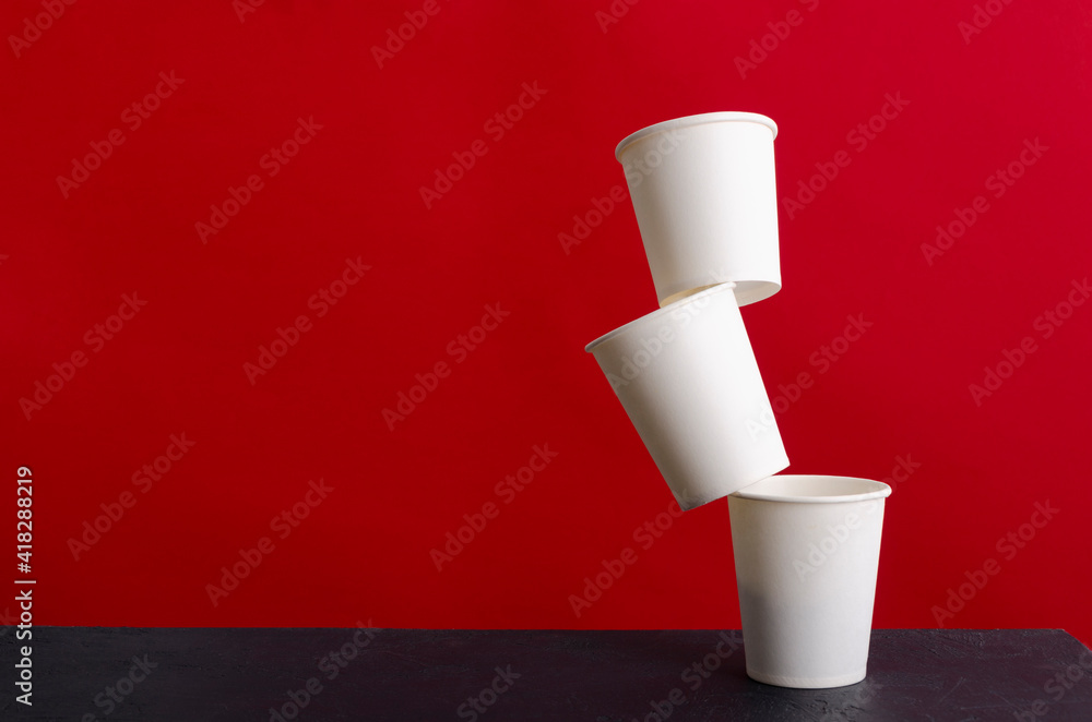 Levitation of white paper cup on the black table against red wall.Empty space Levitation of white paper cup on the black table against red wall.Empty space