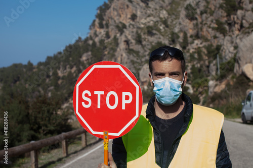 Road maintenance worker during the coronavirus pandemic, on a road with a stop sign and reflective vest