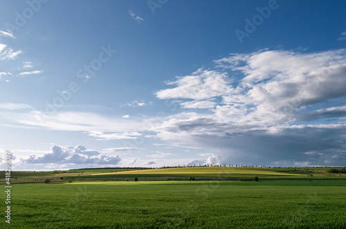 Wonderful rural area of Eastern Ukraine in spring. Beautiful view of green fields in spotty light under big cloud sky. Agricultural fields stretch to the horizon.