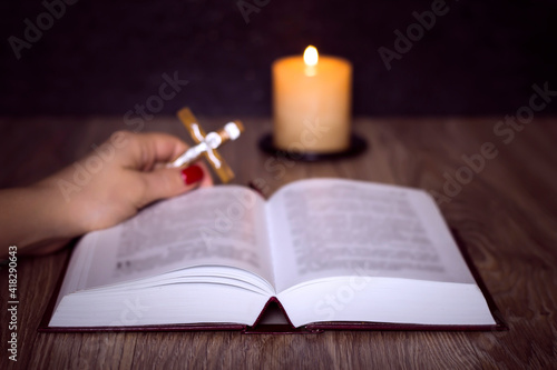 Female hand with a cross and a bible near the candle. Prayer