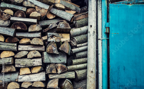 Wooden firewood stacked near a blue door. photo