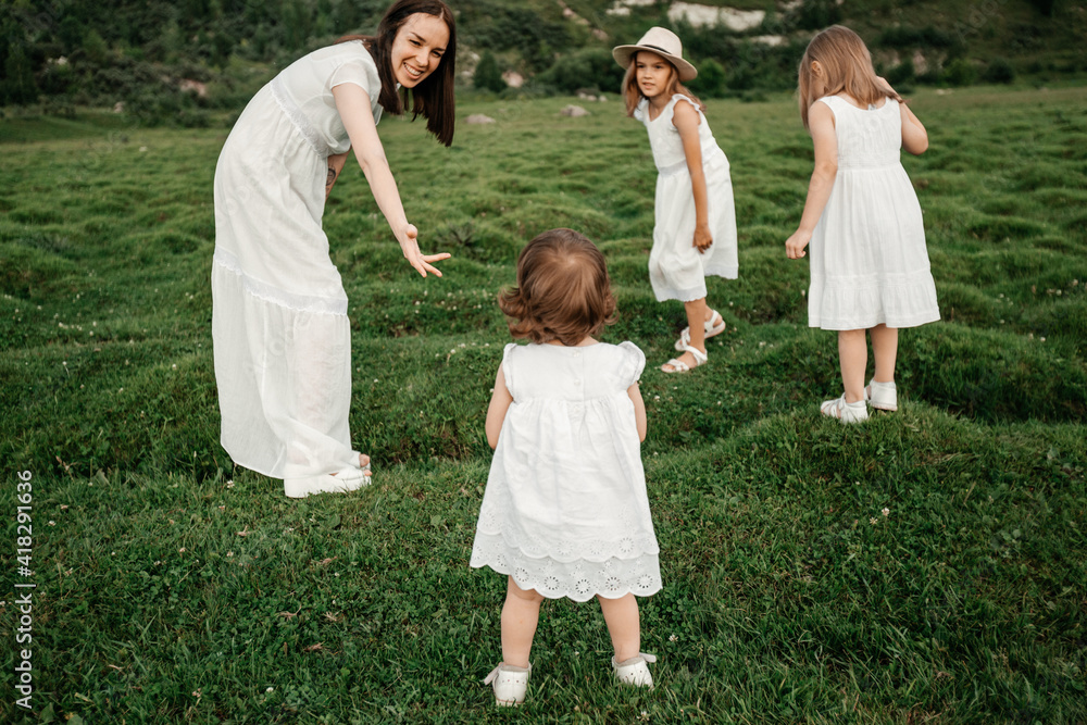 Naklejka premium Happy young family: mother and three daughters in white clothes spending time together outside in green nature.