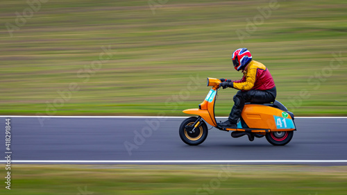 A panning shot of a racing moped as it circuits a track.