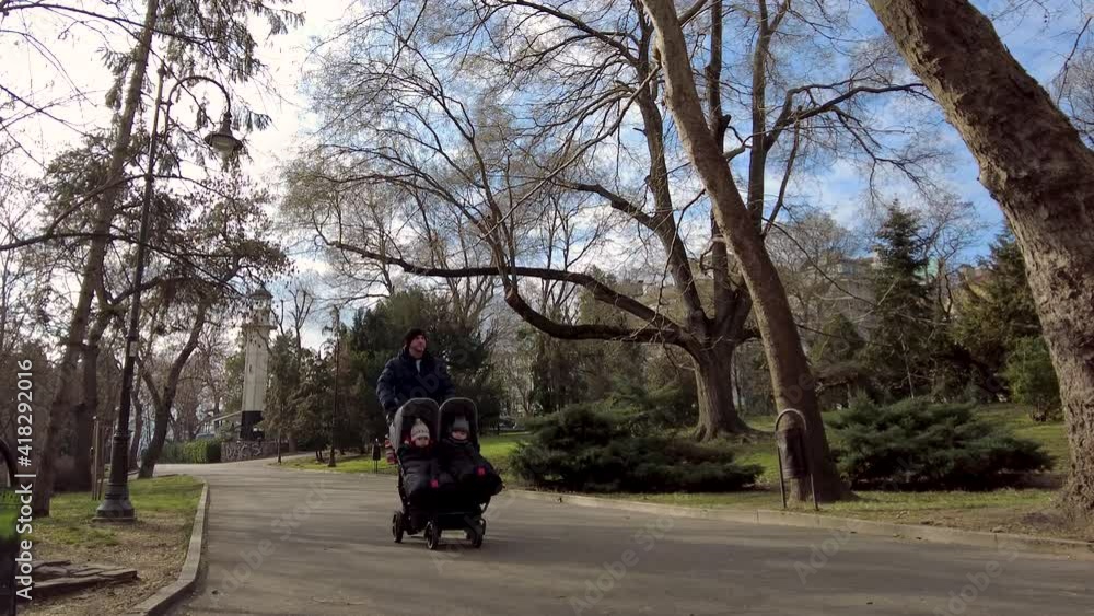 Father with kids in double stroller in a park. Man pushing twins stroller, pram.
Father with kids in double stroller in a park. Man pushing twins stroller, pram.