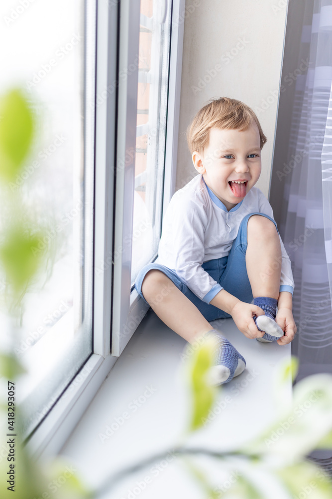 a child boy looks out of the window sitting on the window sill of the house a child boy looks out of the window sitting on the window sill of the house